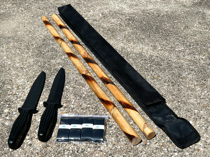 Kali Starter Kit laid out diagonally: pair of rattan sticks, two rubber training knives, grip tape, and black carrying case