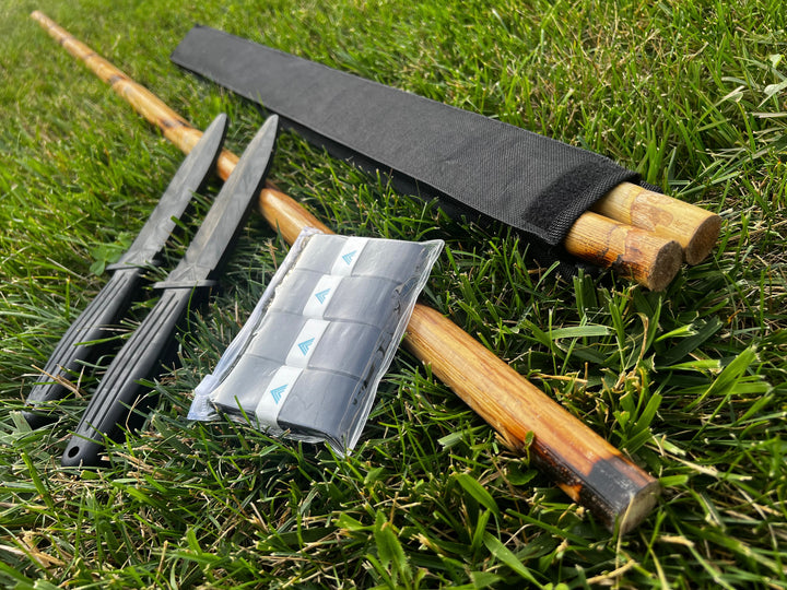 Complete Starter Kit laid out on grass: rattan staff, rattan sticks, rubber training knives, and grip tape